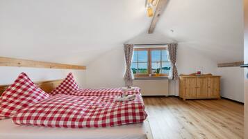 Ein Schlafzimmer mit Holzbalkendecke, einem fenster mit Vorhängen, einem Holzschrank und einem Bett mit Karomuster-Bettwäsche.