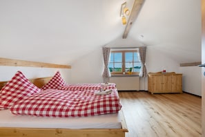 A bedroom with a wooden ceiling, a window with curtains, a wooden cabinet, and a bed with checkered bedding.