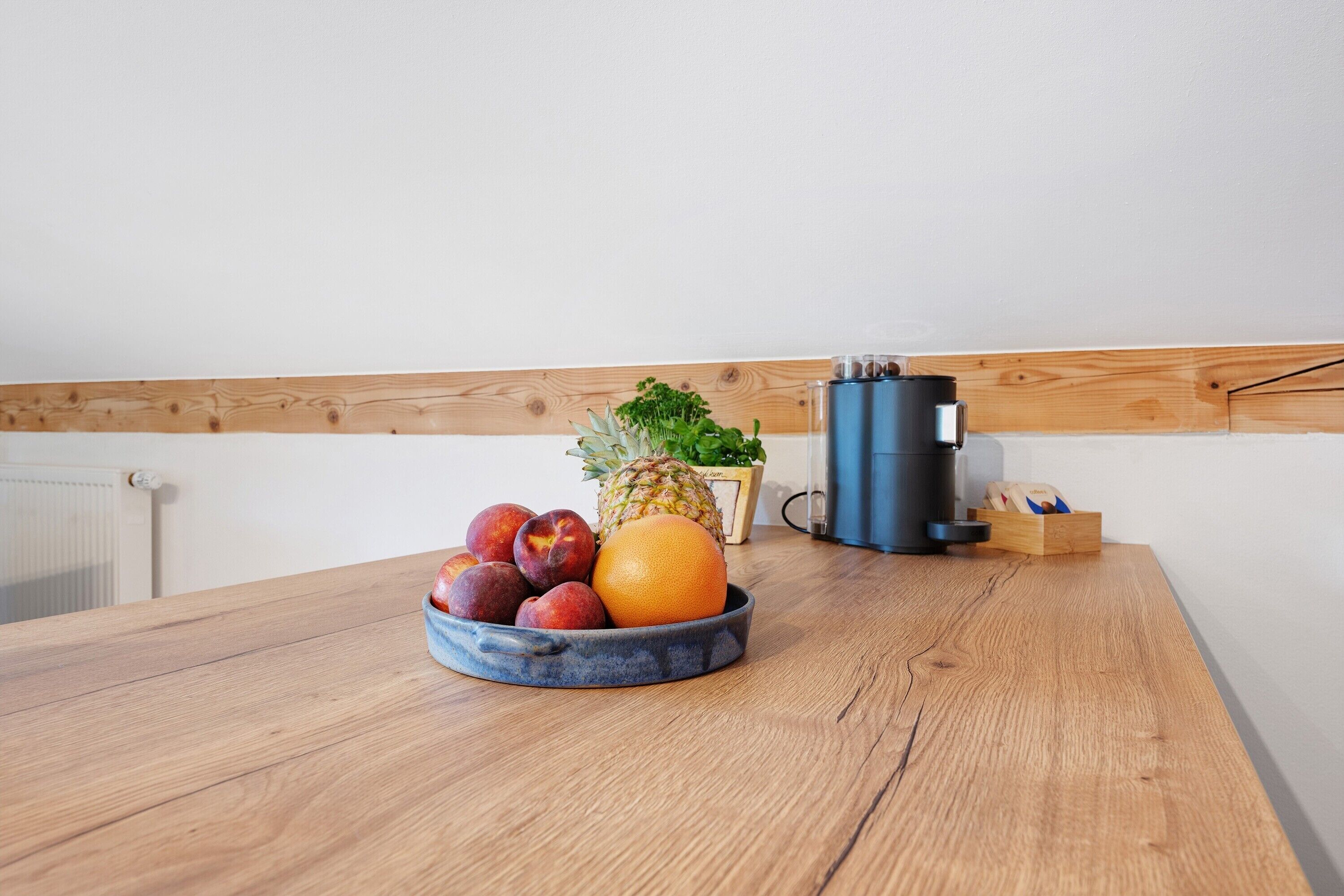 A wooden table with a fruit bowl containing apples, a pineapple, and an orange.