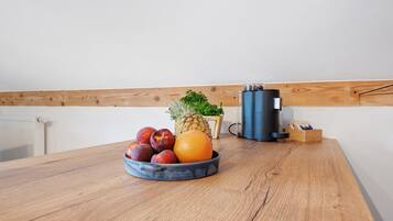 A wooden table with a fruit bowl containing apples, a pineapple, and an orange.