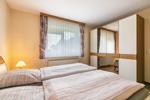 A hotel room with two beds, a window with curtains, a radiator, a desk, and a mirror. - Apartment 'Ilse' with Private Terrace, Shared Garden and Wi-Fi (Schülperweide)