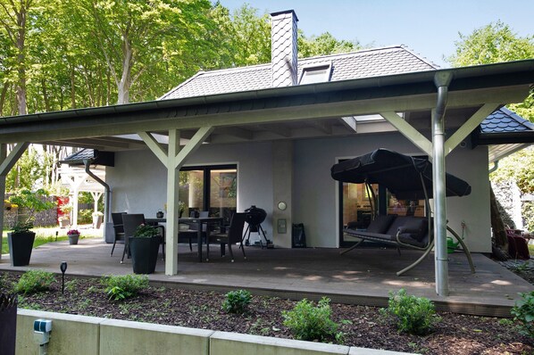 A covered patio with outdoor seating, a grill, and a view of the house.