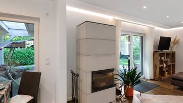 A modern living room with a fireplace, a dining area with outdoor view, and a TV stand.
