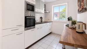 A modern kitchen with white cabinetry, a built-in oven, a microwave, and a window with a view of greenery outside. - Casa Di Napolitano – Nature & Relaxation by Lake Constance (Radolfzell am Bodensee)