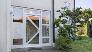 A building entrance with a glass door, a small outdoor area with a potted plant, and a clear sky. - Casa Di Napolitano – Nature & Relaxation by Lake Constance (Radolfzell am Bodensee)