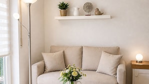 A living room with a sofa, a white coffee table with a vase of flowers, a floor lamp, a side table with a lamp, and a shelf with decorative items. - Casa Di Napolitano – Nature & Relaxation by Lake Constance (Radolfzell am Bodensee)