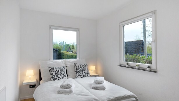 Um quarto com uma cama, duas mesas de cabeceira com luminárias, uma janela com vista para o verde e uma prateleira com plantas em vasos.