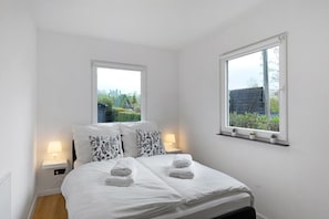 A bedroom with a bed, two bedside tables with lamps, a window with a view of greenery, and a shelf with potted plants. - Apartment 'Oase' with Mountain View, Private Garden and Wi-Fi (Meschede)