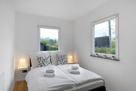 A bedroom with a bed, two bedside tables with lamps, a window with a view of greenery, and a shelf with potted plants.. Apartment 'Oase' with Mountain View, Private Garden and Wi-Fi