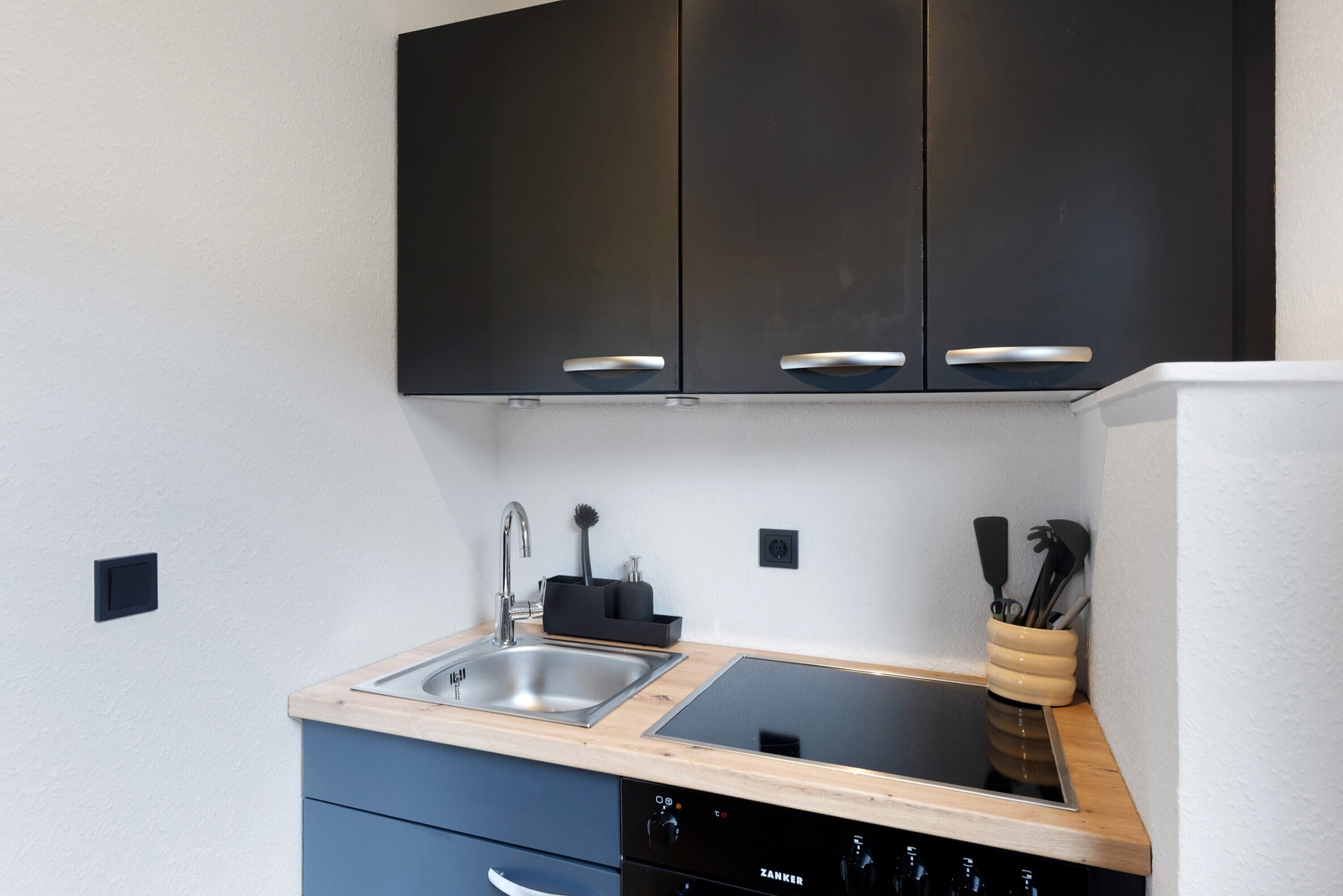 Una cocina con gabinetes negros, un lavamanos de acero inoxidable, una estufa empotrada y un lavavajillas.