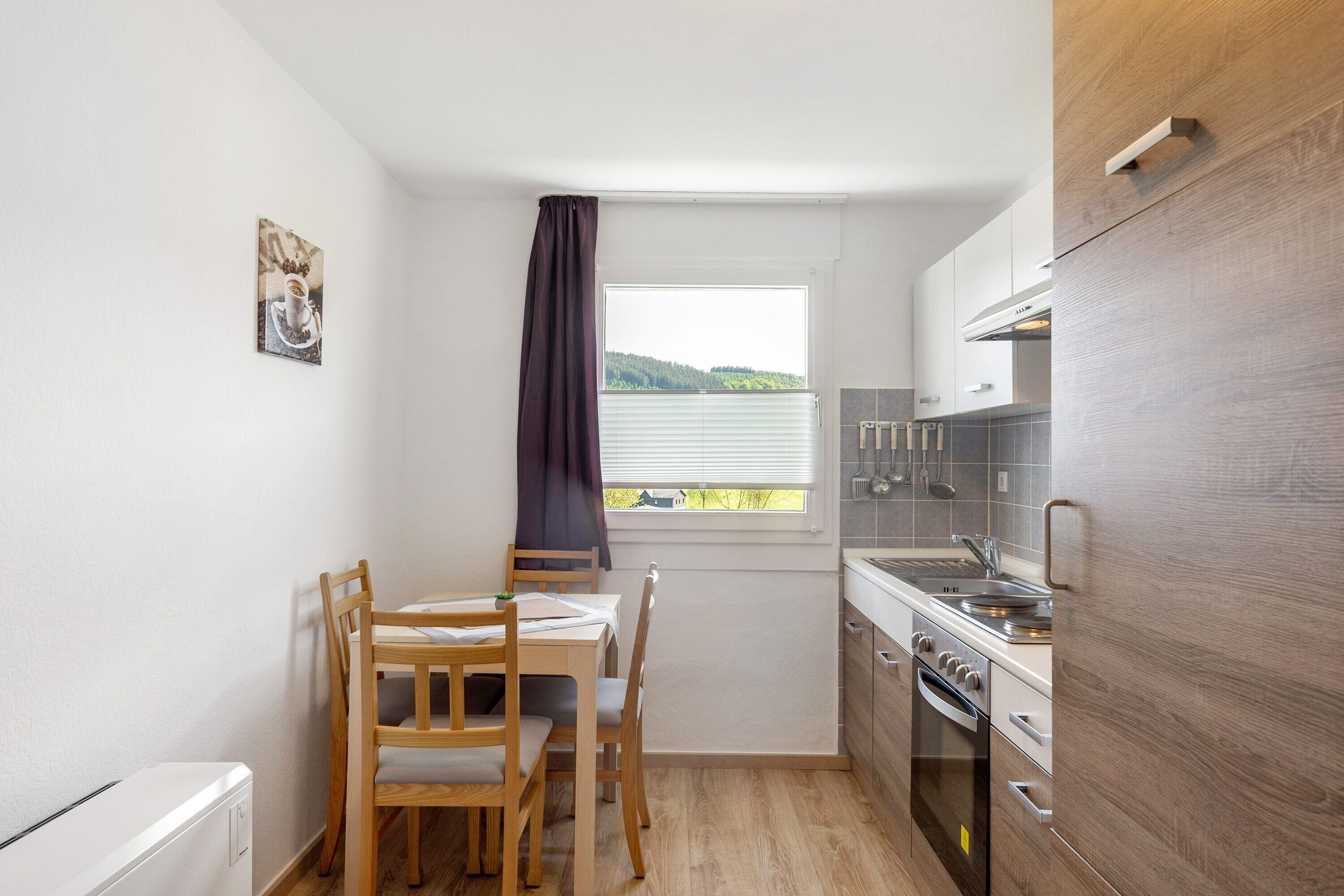 A compact kitchen with a dining table and chairs, a window with a view, and modern appliances.