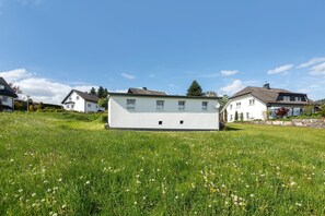 A white building with a flat roof, surrounded by a grassy field with dandelions.