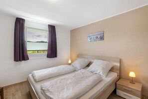 A bedroom with a bed, two bedside tables, a window with curtains, and a painting on the wall.