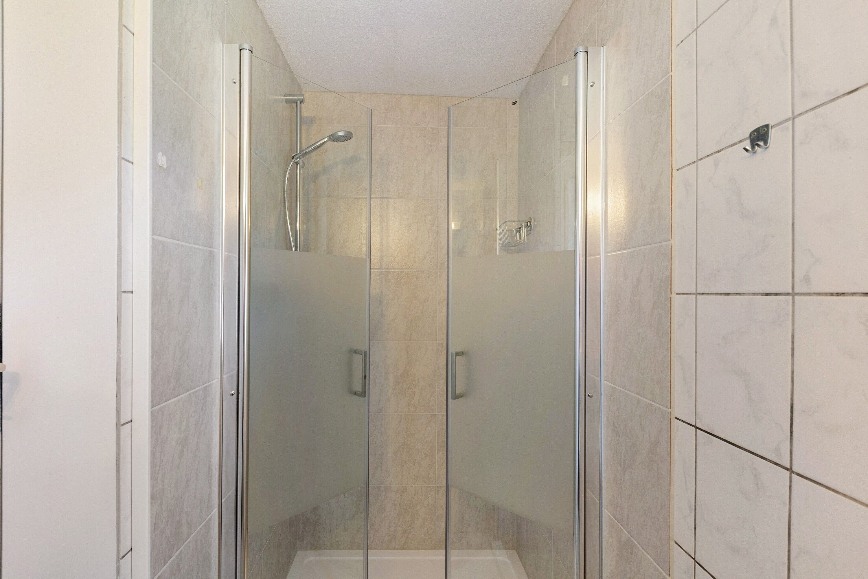 Cabina doccia in vetro con soffione a mano e un altro soffione a mano.