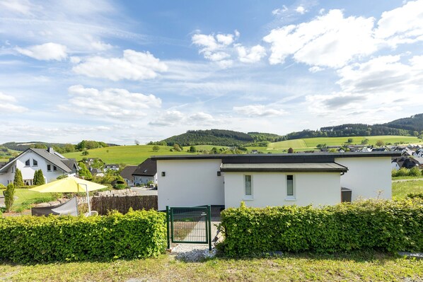 A residential area with a white house, a green gate, and a clear sky.