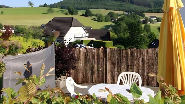 A backyard with a wooden fence, white chairs, and a yellow umbrella.