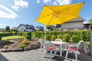 An outdoor patio with a table and chairs, a yellow umbrella, and a well-maintained garden.