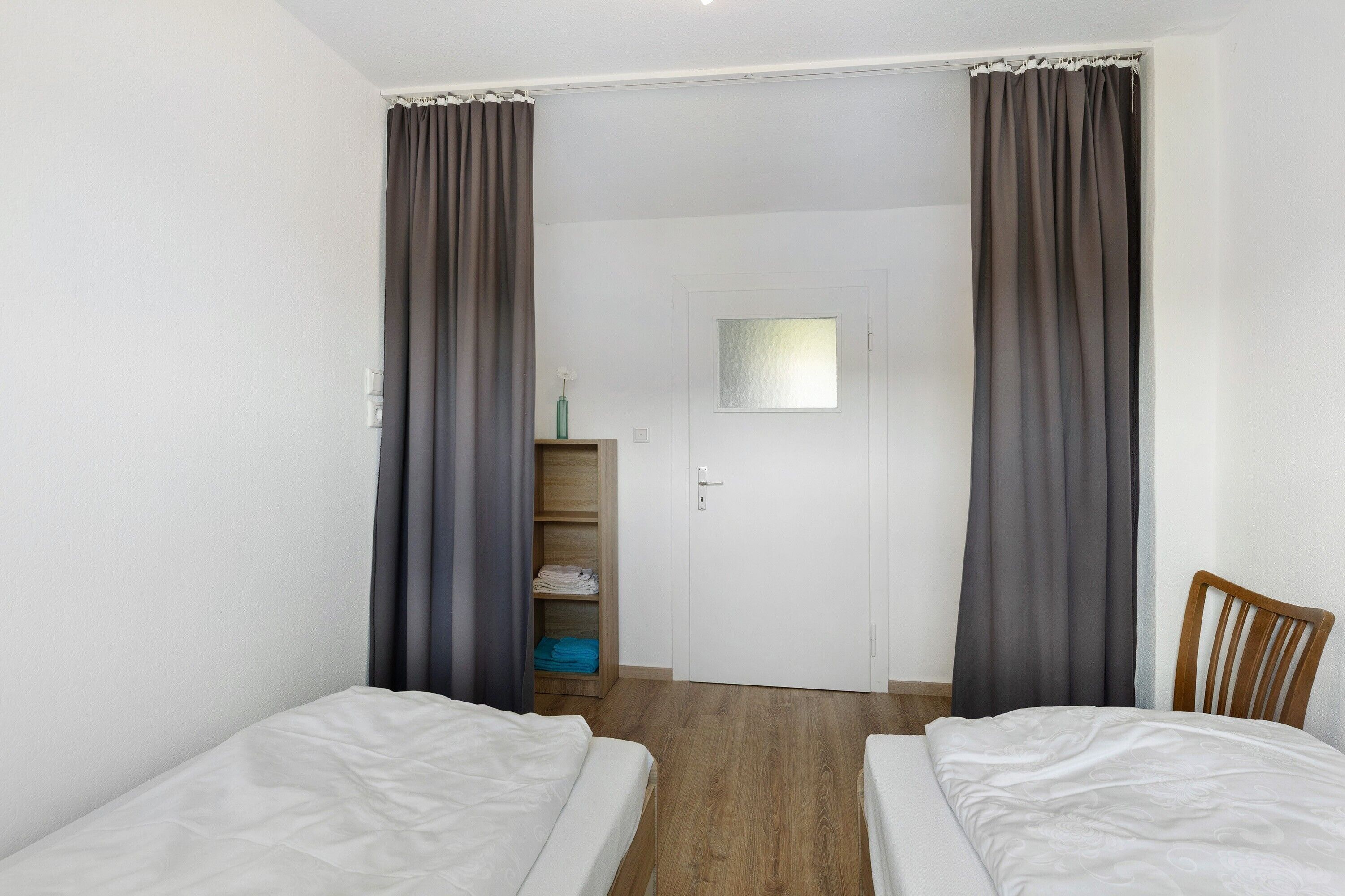 A room with two beds, a wooden wardrobe, and a door with a window.