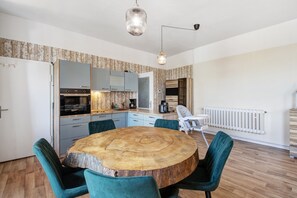 Une cuisine moderne dotée d’un îlot central, d’appareils électroménagers intégrés et d’un coin repas avec une table ronde en bois et des chaises de couleur turquoise.