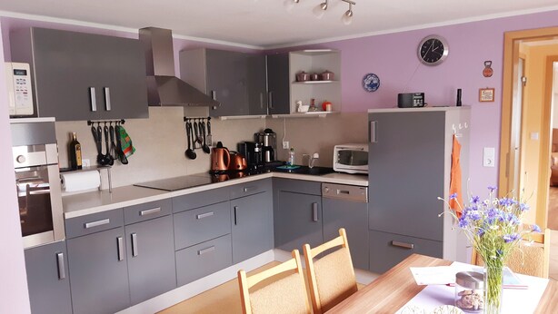 A modern kitchen with grey cabinets, a wooden dining table, and a microwave. - Holiday Home 'Waldblick' with Private Terrace, Private Garden and Wi-Fi (Reinharz)