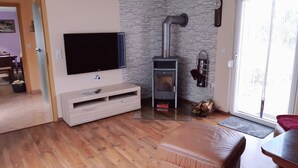 A living room with a TV, a fireplace, a sofa, and a dining area. - Holiday Home 'Waldblick' with Private Terrace, Private Garden and Wi-Fi (Reinharz)
