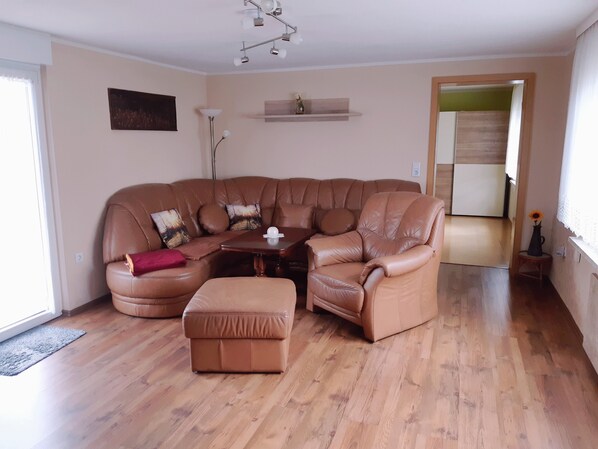 A living room with a brown leather sectional sofa, a matching ottoman, a small wooden coffee table, and a floor lamp.