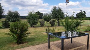 A paved outdoor area with a metal table, surrounded by greenery and a fence. - Holiday Home 'Waldblick' with Private Terrace, Private Garden and Wi-Fi (Reinharz)