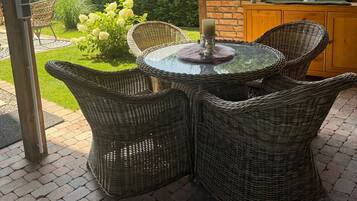 A covered outdoor seating area with wicker furniture, a glass table, and a hanging light fixture.