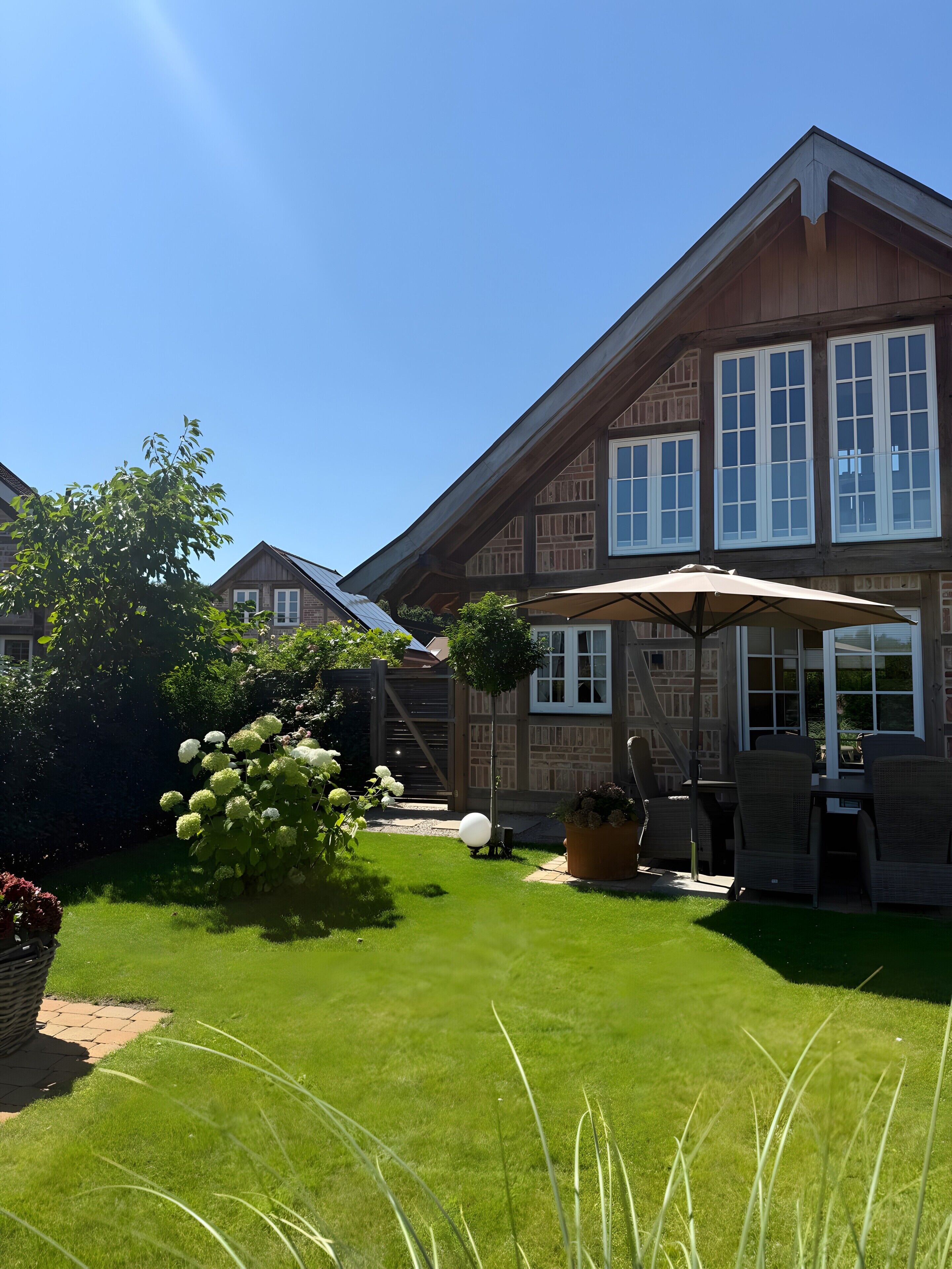 A wooden house with a well-maintained lawn, outdoor furniture, and a large umbrella.