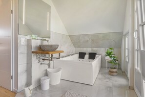 Ein modernes Badezimmer mit einer freistehenden Badewanne, einem großen Spiegel und einem Holzbodenregal.