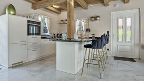 Eine moderne Küche mit weißen Schränken, einer zentralen Kochinsel mit Barhocker und Holzbalken an der Decke.