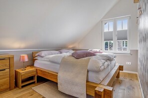 Ein Schlafzimmer mit schrägem Dach, einem Bett mit Kissen, einem Nachttisch mit Lampe und einem Fenster.