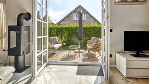 Ein offener Wohnbereich mit Fernseher, Sitzgelegenheit und Blick auf ein Haus durch Glastüren.