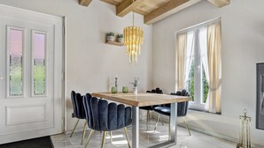 Ein Essbereich mit einem Holztisch, dunkel gepolsterten Stühlen, einer Chandelierleuchtre und einem großen Fenster mit Vorhängen.