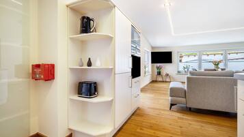 Een moderne woonkamer met een ingebouwde televisie, een bank en een koffiezetapparaat op een wit kastje.