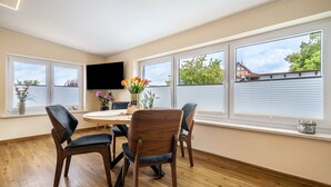 A dining area with a round table, four chairs, a vase with flowers, and a TV mounted on the wall.