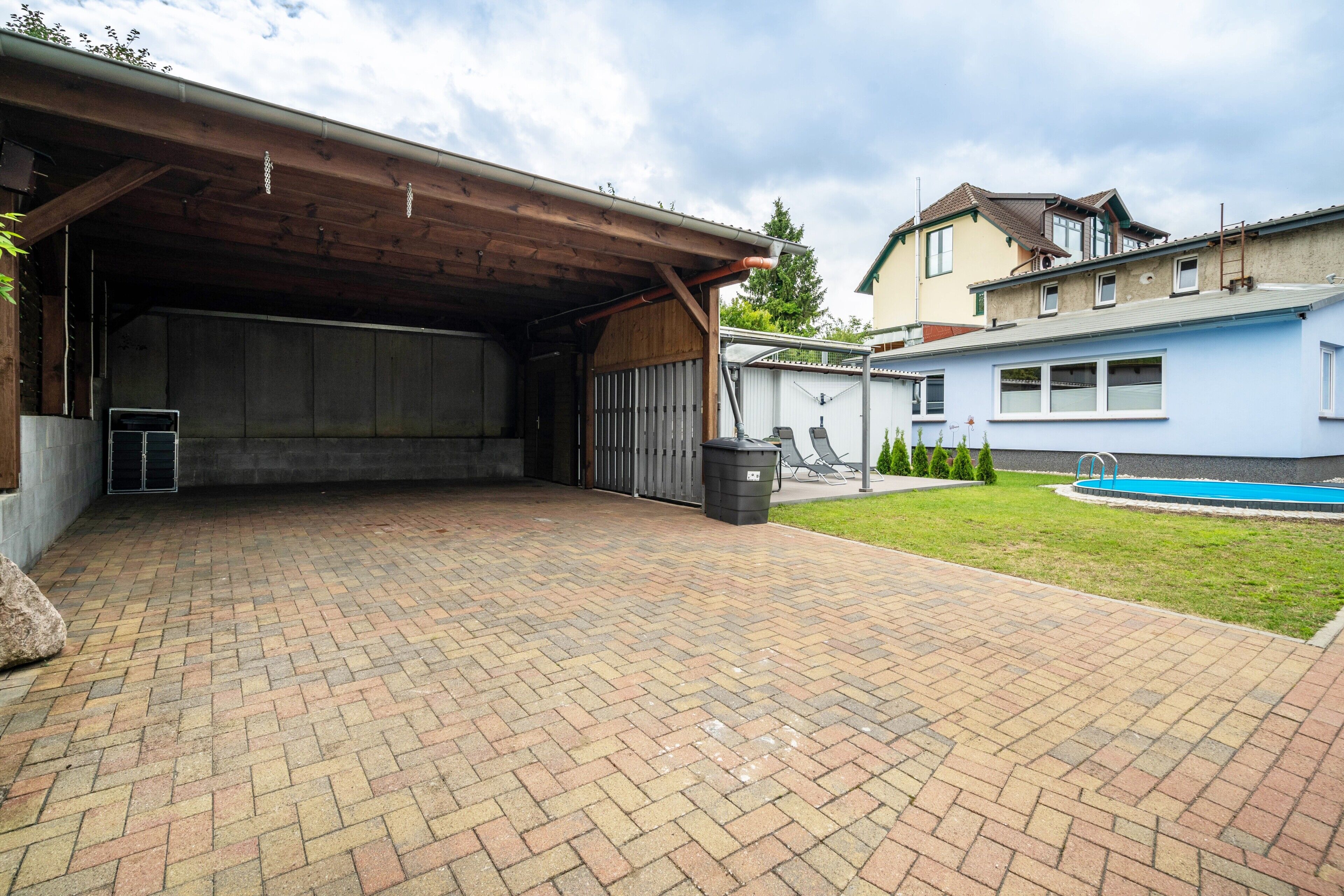 A covered patio area with a brick floor, a metal gate, and a swimming pool in the background.