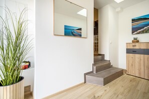 En trappa som leder upp till andra våningen, en krukväxt, ett träskåp och en inramad tavla på väggen.