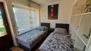 Una camera da letto con due letti, una finestra con persiane, un quadro raffigurante un faro e un armadio bianco.