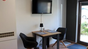 Una stanza con TV a schermo piatto montata a parete, un tavolino con due sedie, una lampada e una finestra vista esterna.