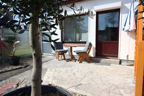 Eine Terrasse im Freien mit Tisch, Stühlen, einem Blumentopf und einer Tür mit Fenster.