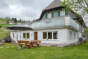 Ein zweistöckiges Haus mit Balkon, einer Holzbank und einem Tisch mit Sonnenschirm.