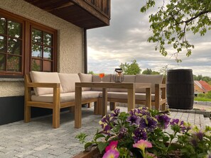 An outdoor seating area with a wooden table and sofa, surrounded by potted plants.