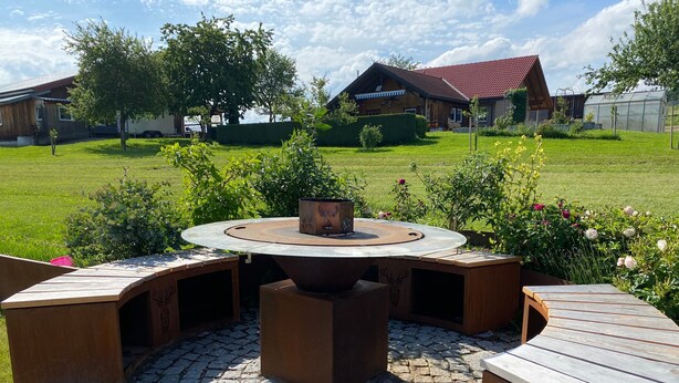 A circular wooden outdoor seating area with a fire pit, surrounded by a cobblestone patio.