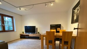 A modern living room with a flat-screen TV, wooden dining table, and chairs.