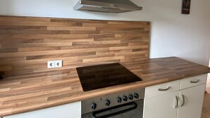 A kitchen with a wooden countertop, a stove, a range hood, and a built-in oven.