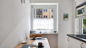Una cocina pequeña con una mesa preparada para dos, una ventana con vistas a edificios y un calendario en la pared.