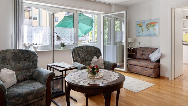 Una sala de estar con sofá, sillas, una mesa con un florero y un mapa mundial en la pared.