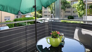 Un balcón con una sombrilla verde, una mesa de cristal y una planta en maceta.