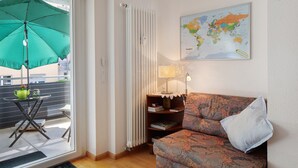 Una habitación con un sofá, una mesita con un paraguas verde, un radiador, una lámpara y un mapa mundial en la pared.